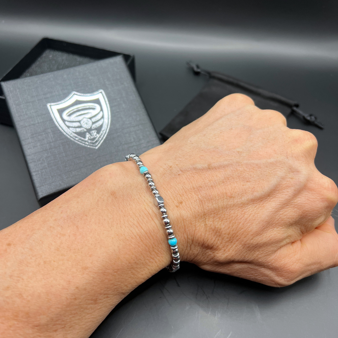 Close-up of Aqua Pulse bracelet worn on wrist with Armoured Elegance box and pouch in background