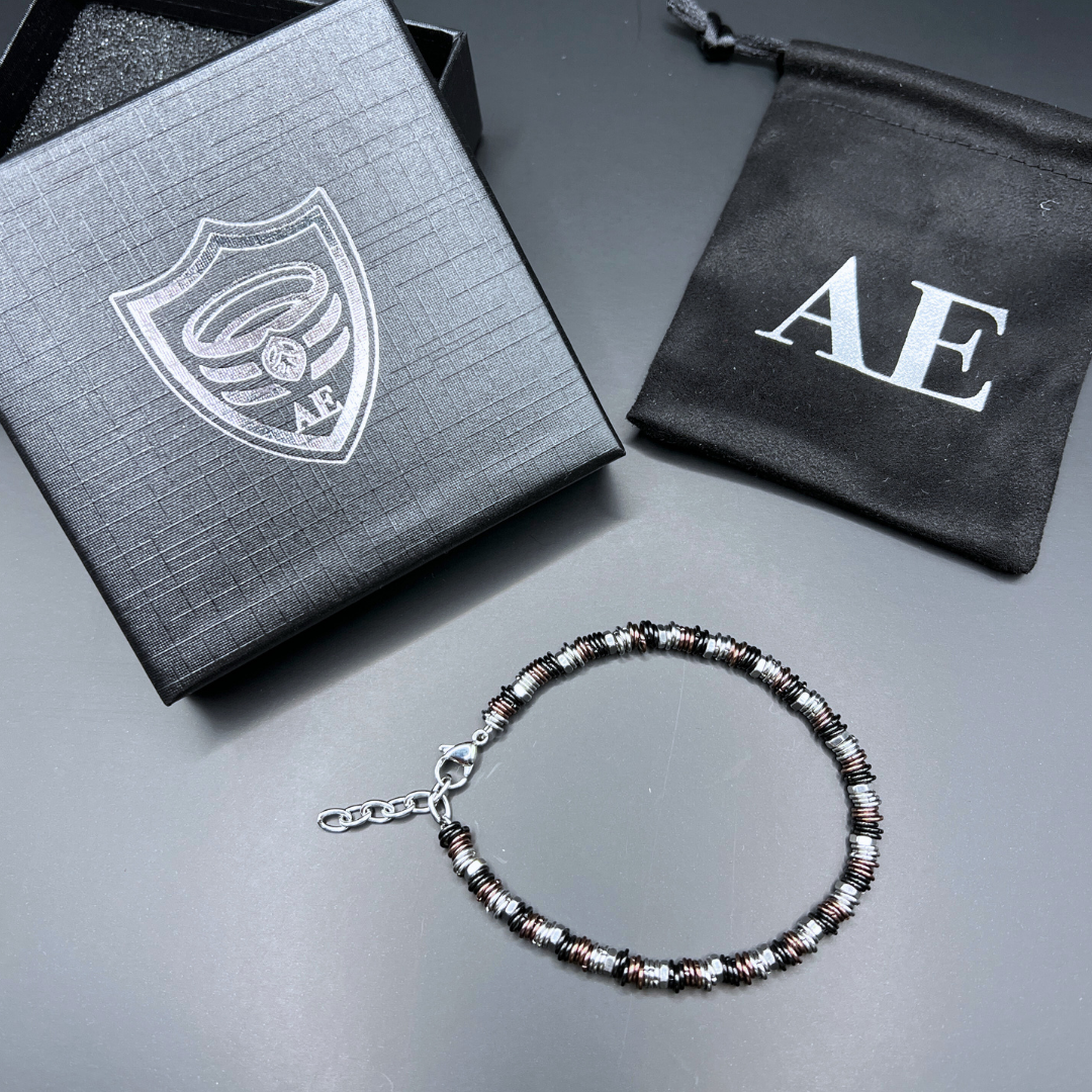 Side angle of Industrial Torque copper edition bracelet beside Armoured Elegance packaging and velvet pouch