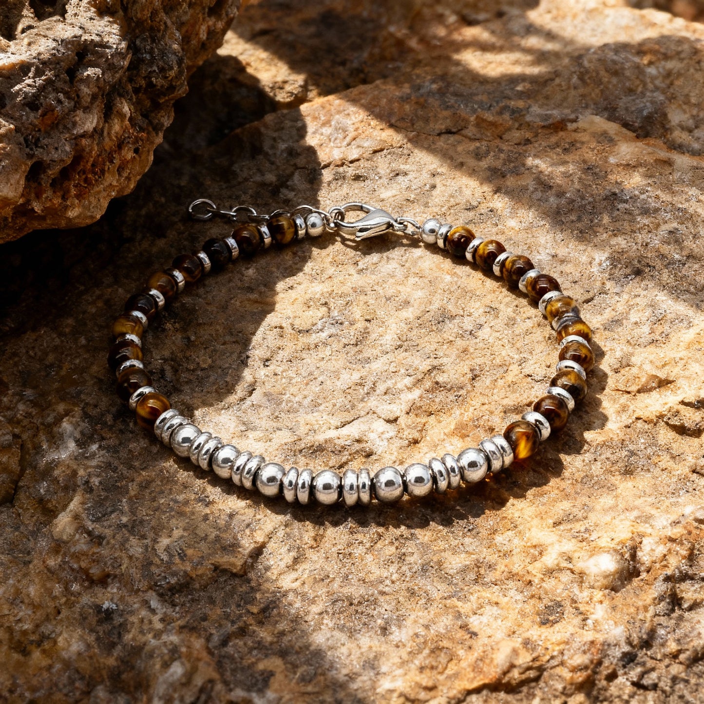 Tiger’s Spirit bracelet displayed on textured rock surface, emphasising the contrast between warm tiger eye stones and sleek stainless steel.