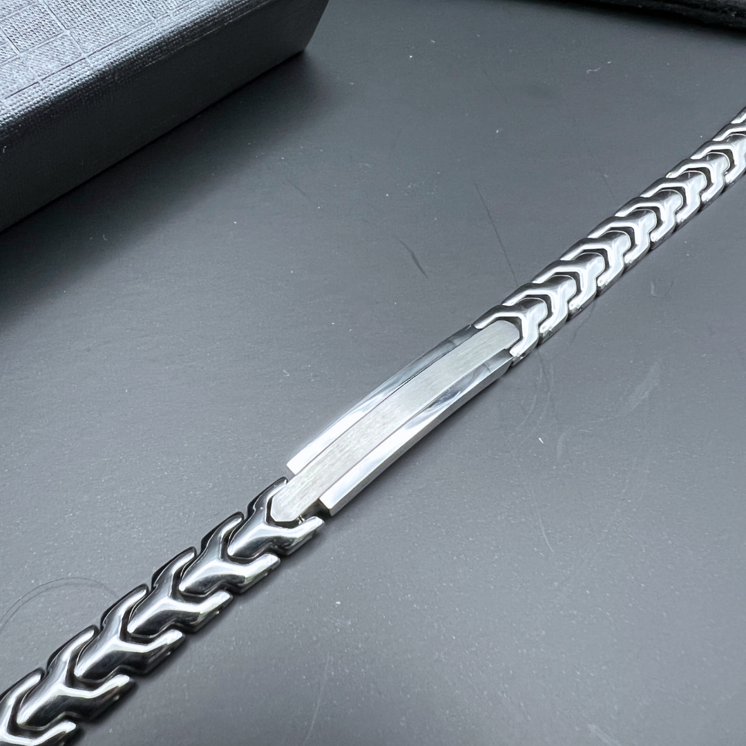 Flat lay of the Aegon bracelet showcasing its full-length geometric chain and brushed stainless steel centerpiece on a dark surface.