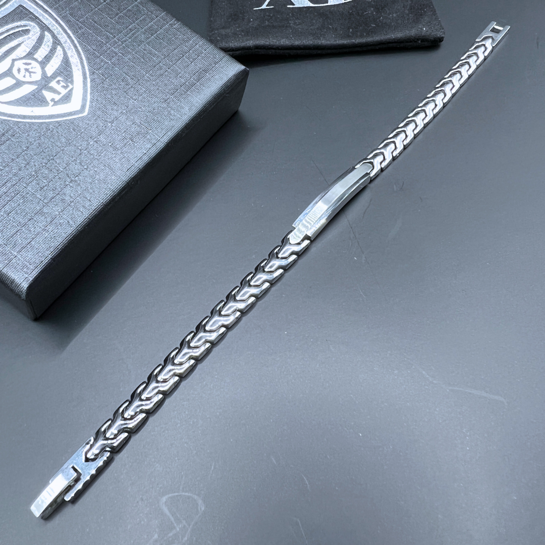 Aegon bracelet displayed fully extended on a dark surface with the Armoured Elegance box and pouch in the background, highlighting its sleek stainless steel link design.