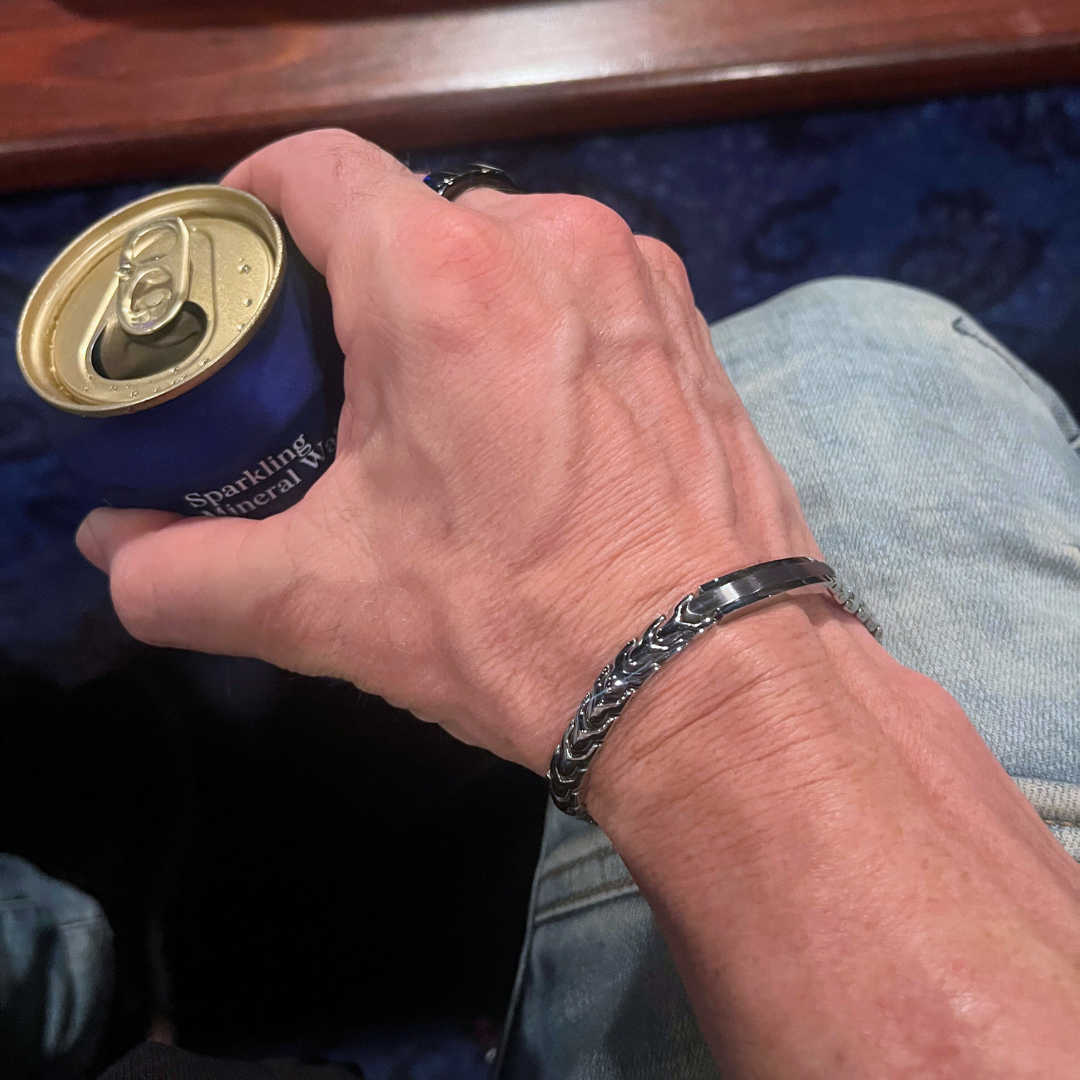Close-up of a man's wrist wearing the Aegon bracelet while holding a can, highlighting the bracelet’s detailed chain pattern and polished metal centerpiece.