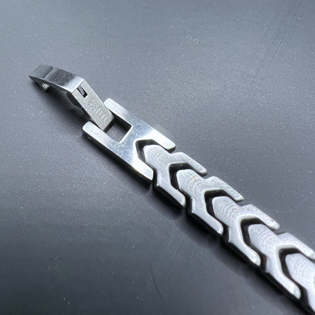 Macro shot of the Aegon bracelet showing the stainless steel (S.STEEL) marking on the clasp against a dark background.