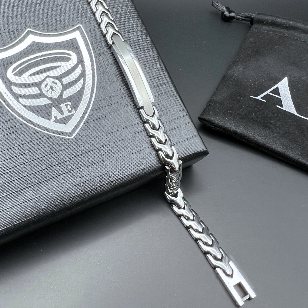 Close-up of the Aegon stainless steel chain bracelet resting on a textured Armoured Elegance gift box with branded pouch in background.