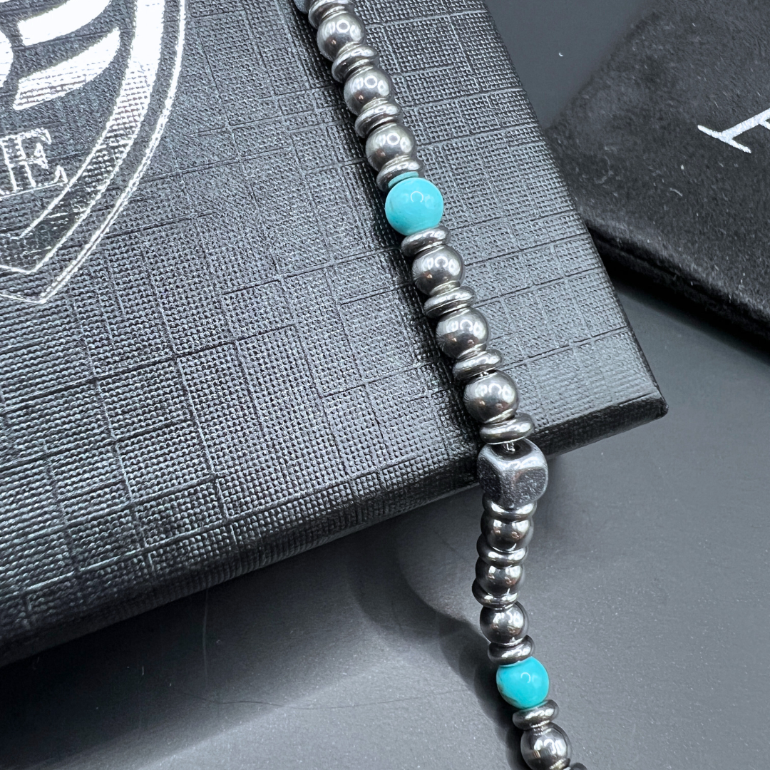 Close-up of Aqua Pulse bracelet showing turquoise stone and polished stainless steel beads on Armoured Elegance box