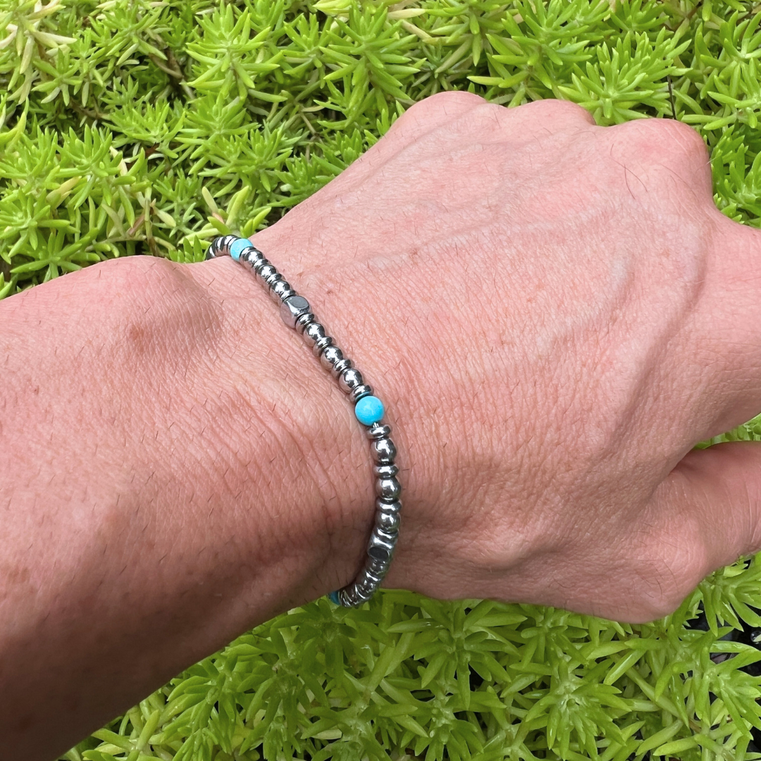 Aqua Pulse bracelet worn on wrist with vibrant green plant background highlighting turquoise and steel beads