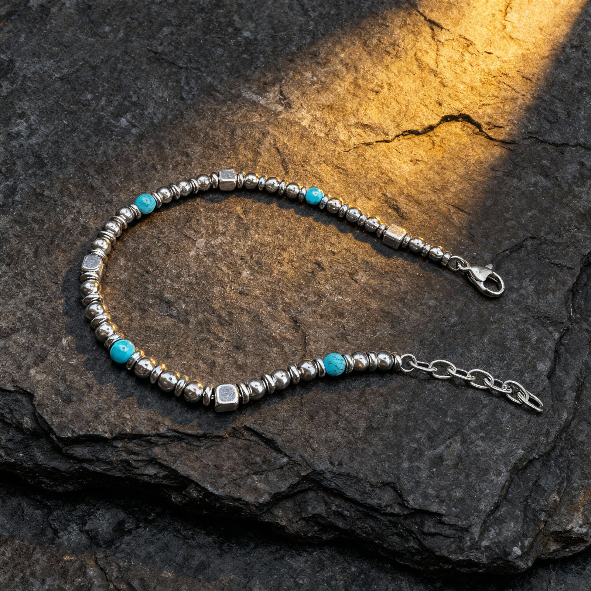 Luxury men’s Aqua Pulse bracelet featuring turquoise natural stone beads and polished stainless-steel spacers displayed on dark rock surface under warm light.