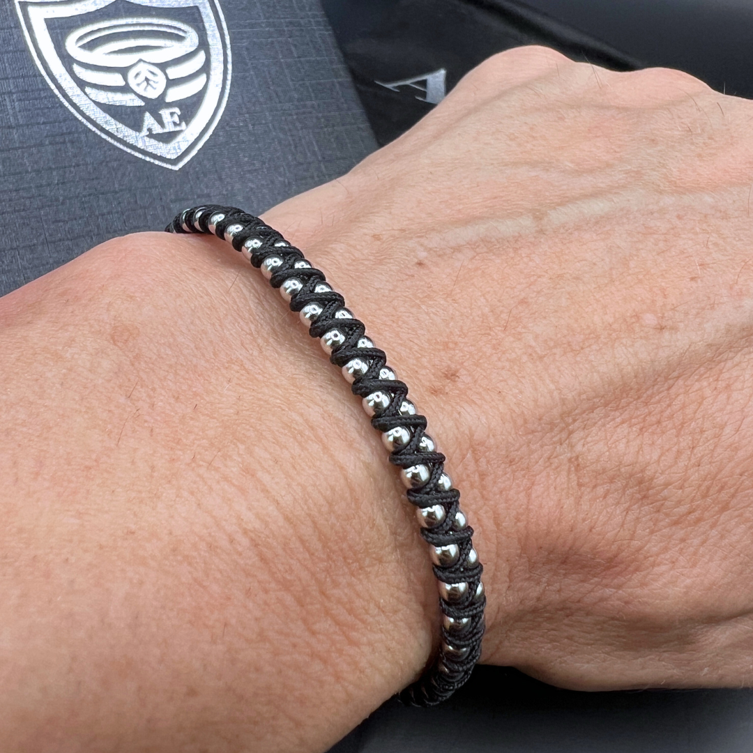 Black Synergy bracelet with woven cord and stainless steel bead design shown on wrist – modern men’s accessory.