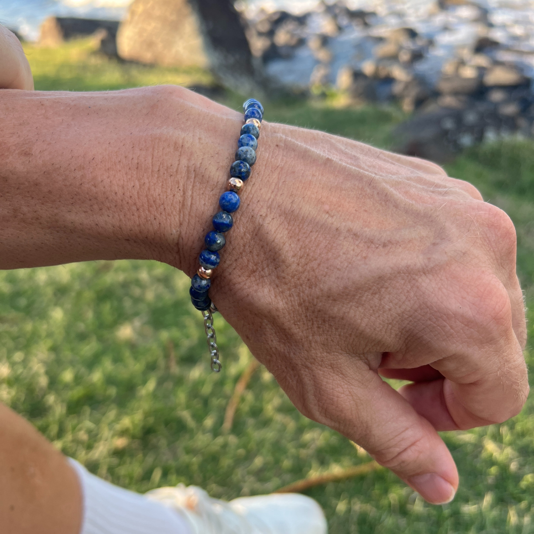 Auric Lineage Cosmic blue bead bracelet worn outdoors near the coast with sunlight on the hand.