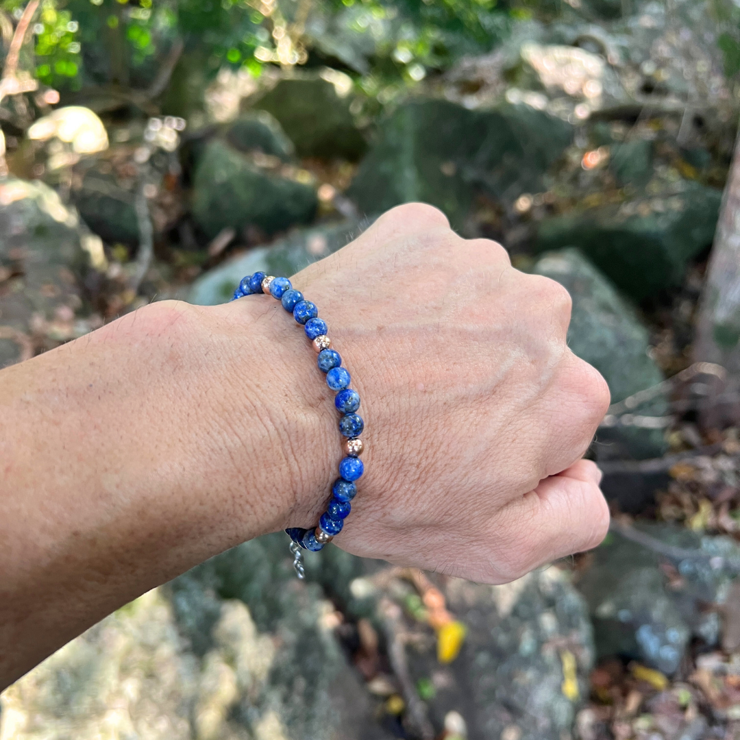 Auric Lineage Cosmic edition blue bead bracelet worn in a natural outdoor setting with rocks and foliage.