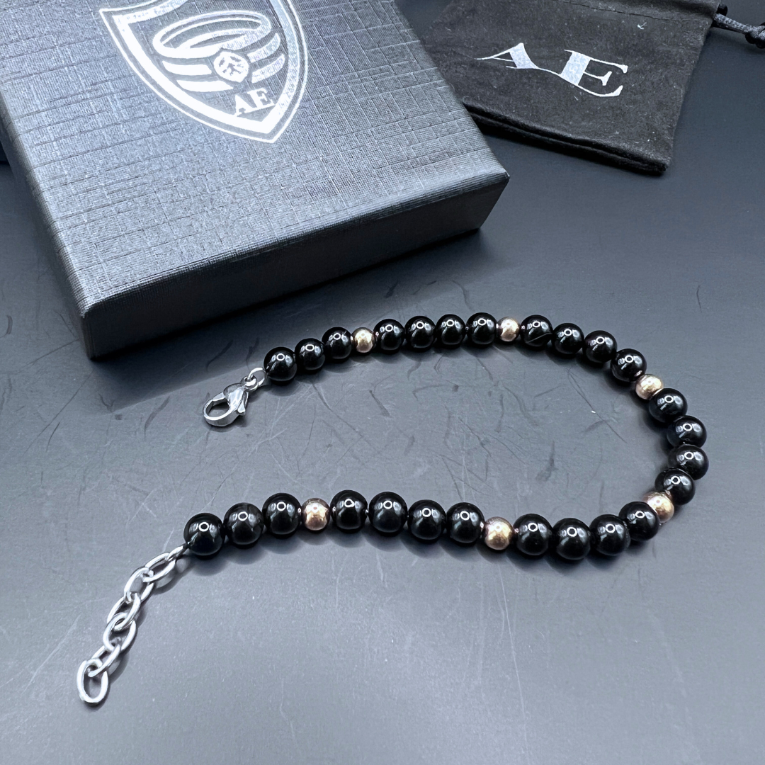 Auric Lineage Shadow edition black bead bracelet displayed flat with gold accent beads and stainless steel clasp.