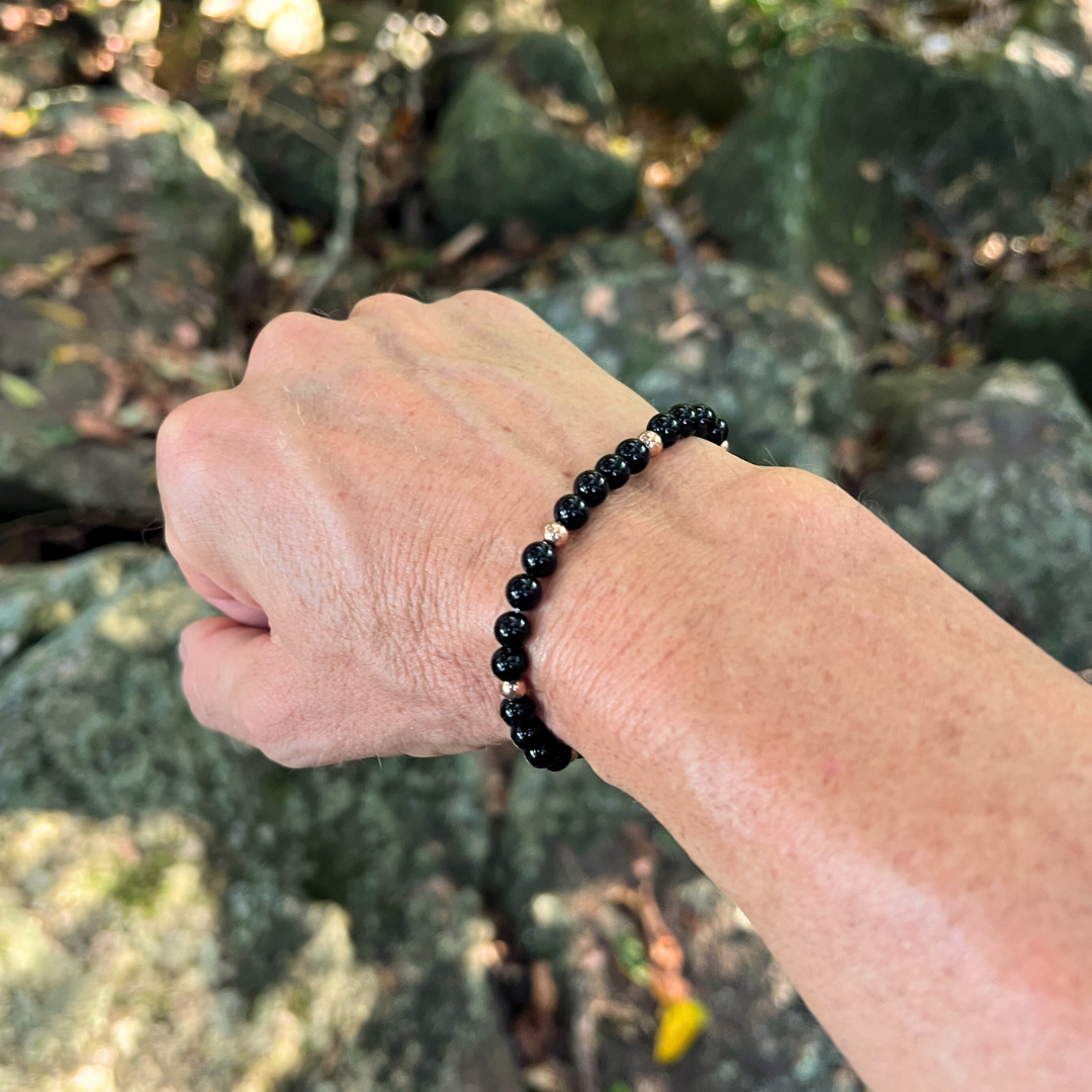Auric Lineage Shadow black bead bracelet worn outdoors among rocks and greenery.