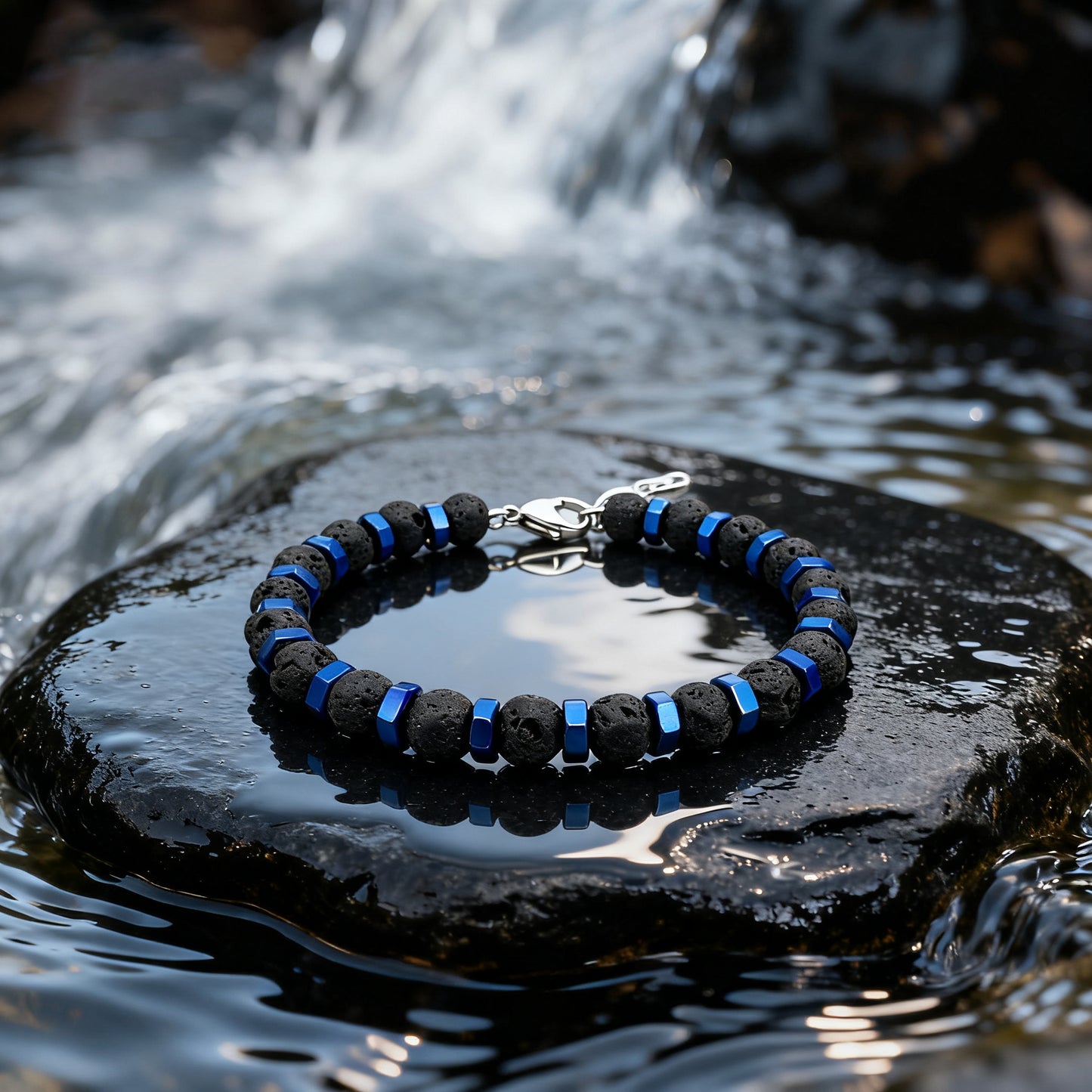 Blue Nexus bracelet photographed outdoors on wet rock with waterfall backdrop, showing contrast between black lava stones and blue metal accents.