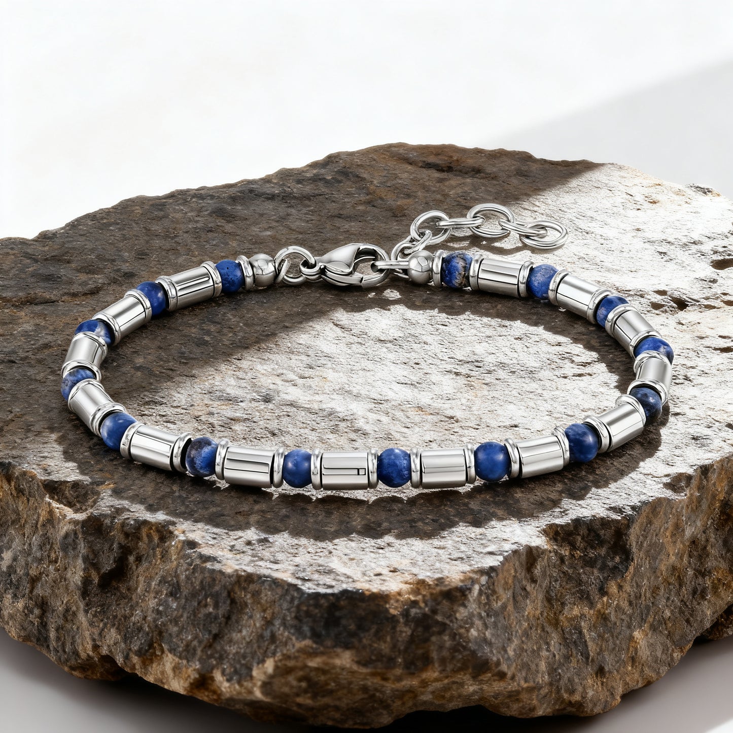 Luxury men’s Earth Pulse bracelet featuring deep blue natural stone beads and polished stainless-steel tubes displayed on rock surface.