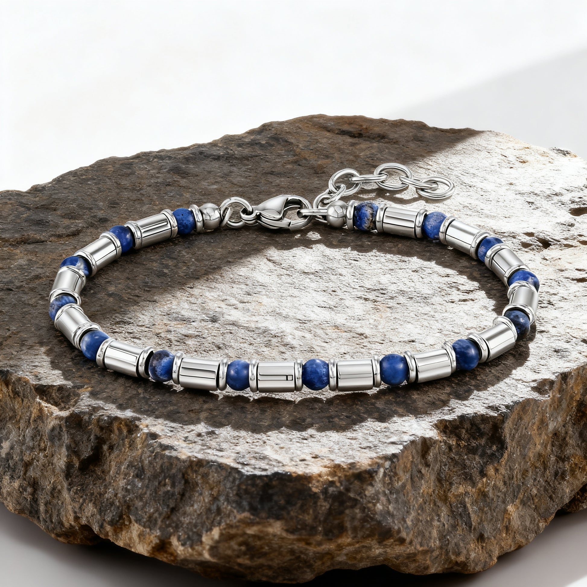 Luxury men’s Earth Pulse bracelet featuring deep blue natural stone beads and polished stainless-steel tubes displayed on rock surface.