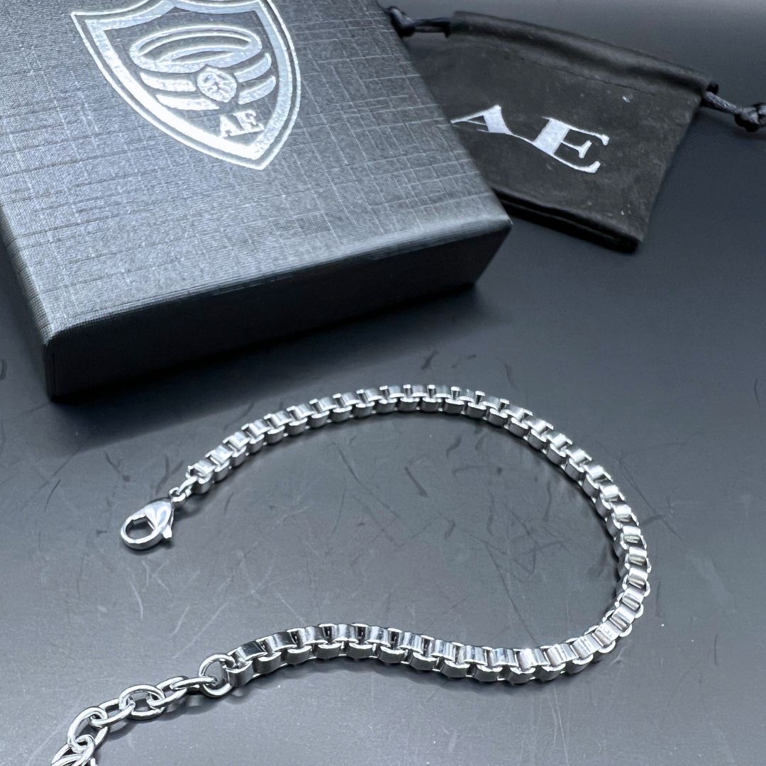 Element stainless steel box-chain bracelet laid flat beside Armoured Elegance packaging.