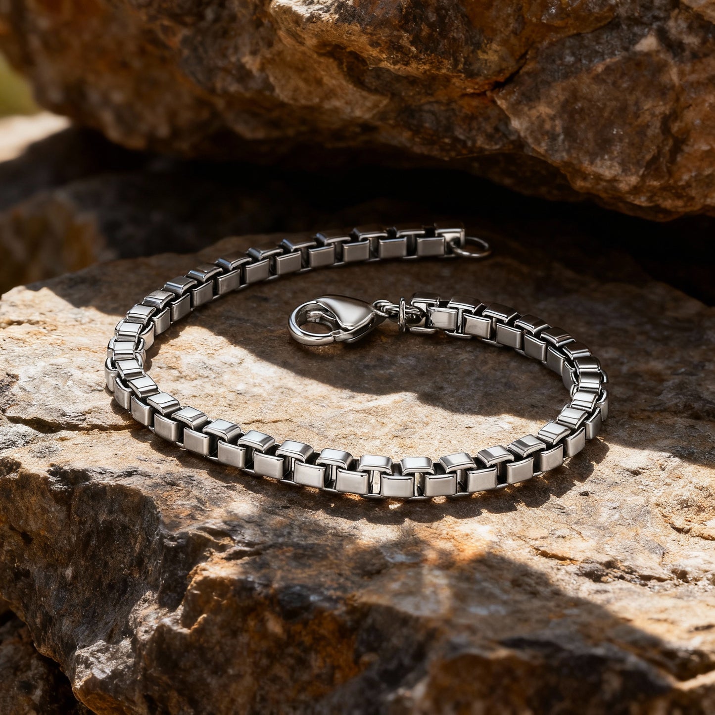 Element stainless steel box-chain bracelet displayed on natural rock under warm sunlight.