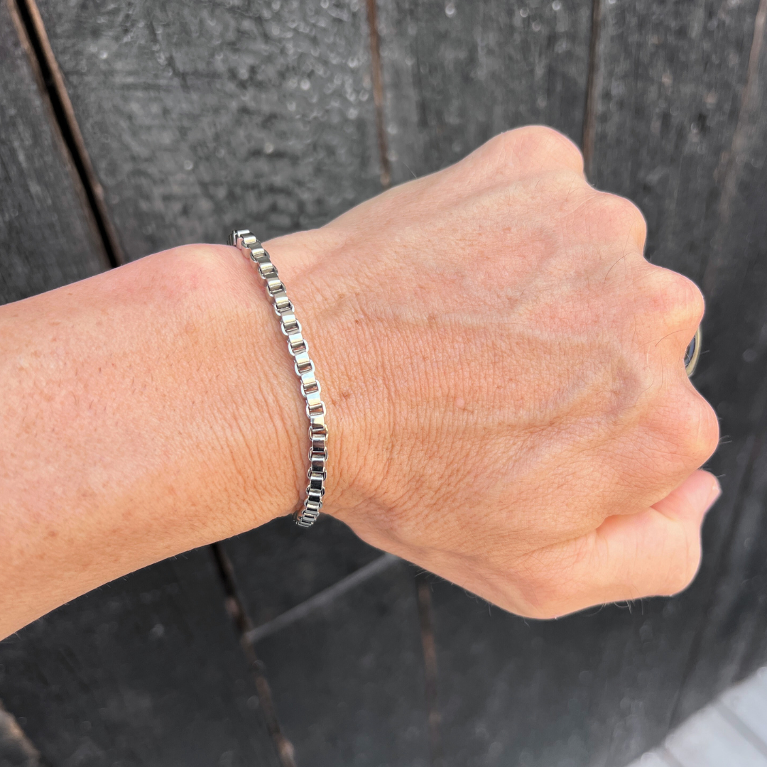Element stainless steel box-chain bracelet worn on wrist against a dark timber background.
