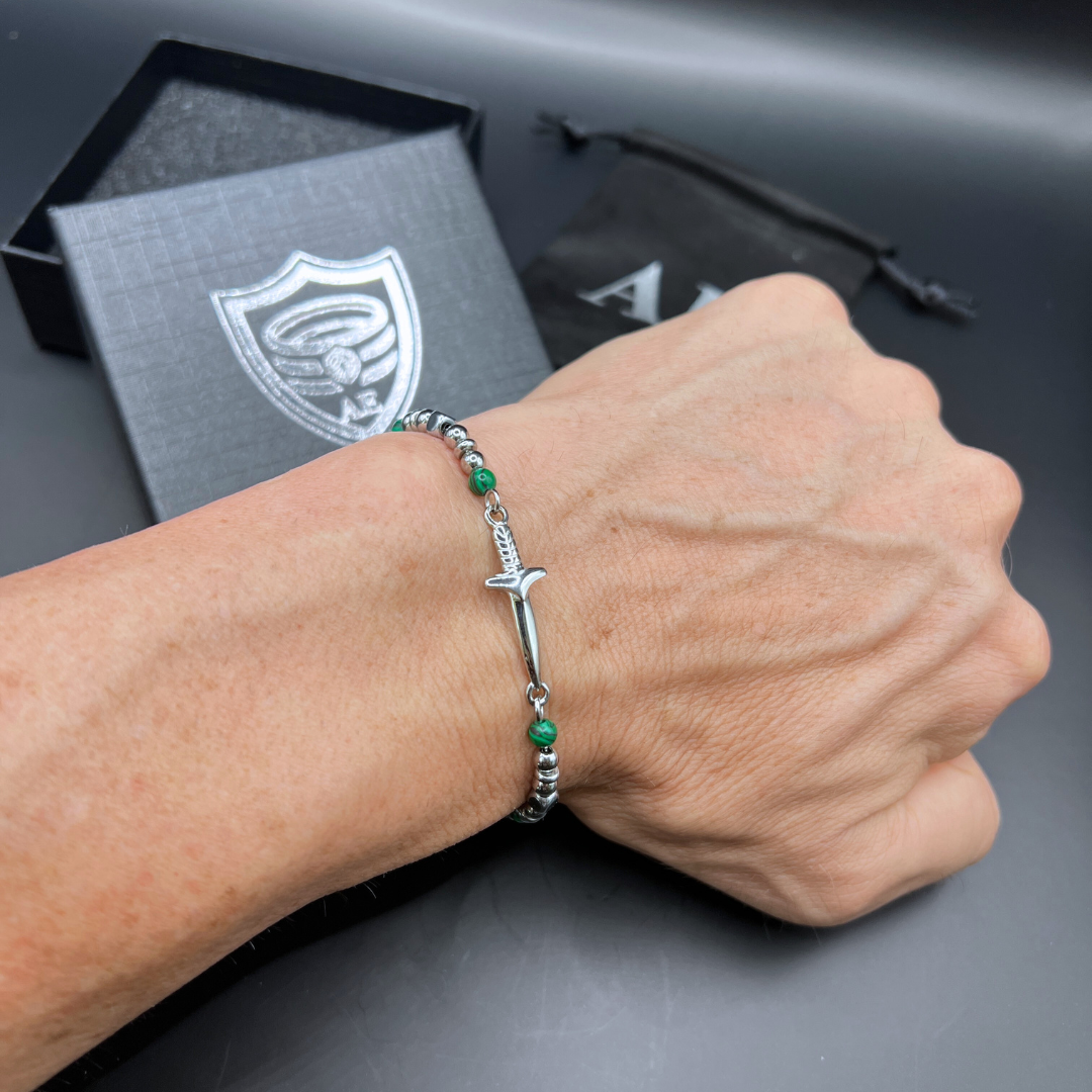 Legion bracelet worn on wrist featuring stainless steel sword charm, polished beads, and green malachite accents.