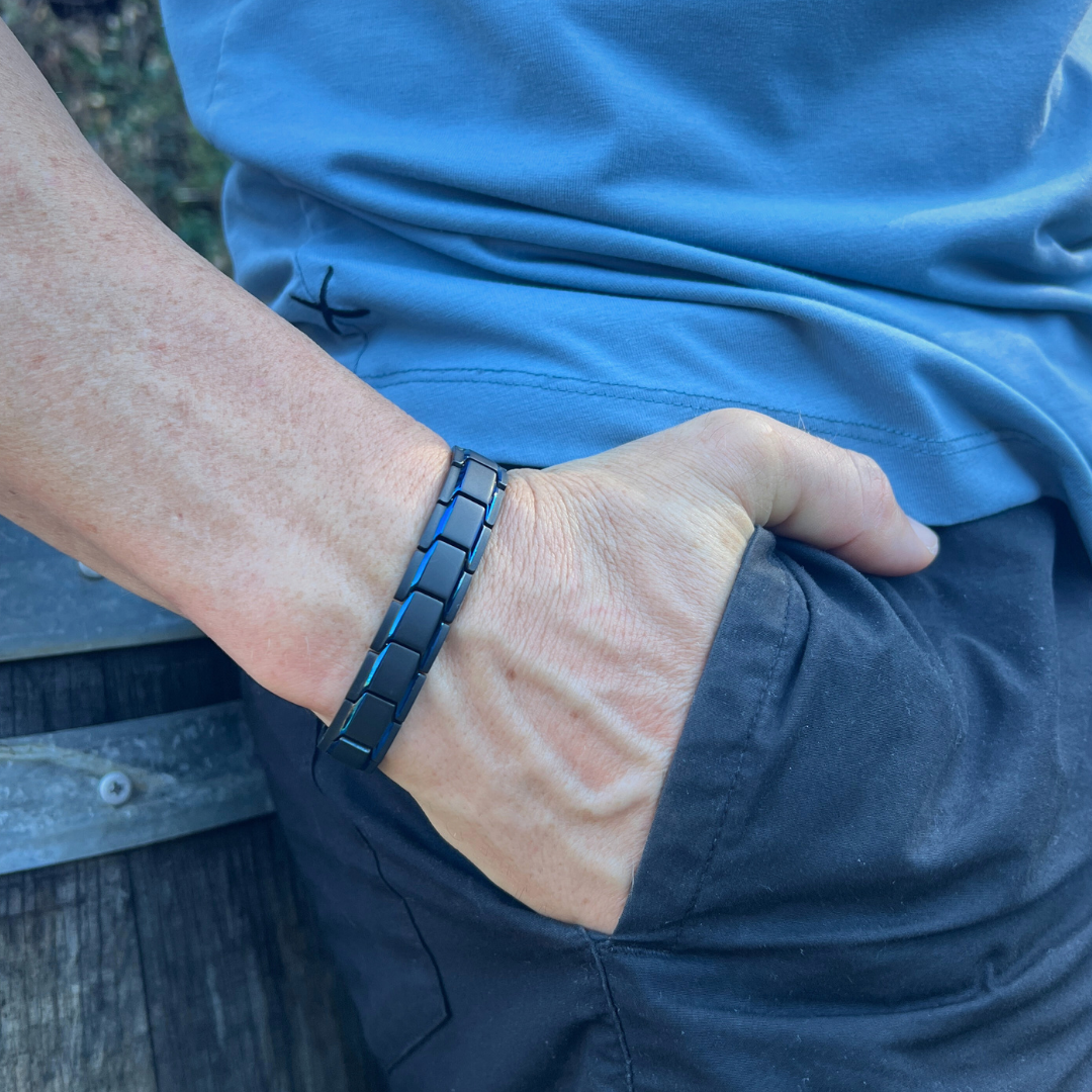 Close-up of a man wearing the Midnight Series black chain link bracelet with his hand in his pocket, showcasing the sleek matte finish in natural light against a casual blue shirt and black pants.