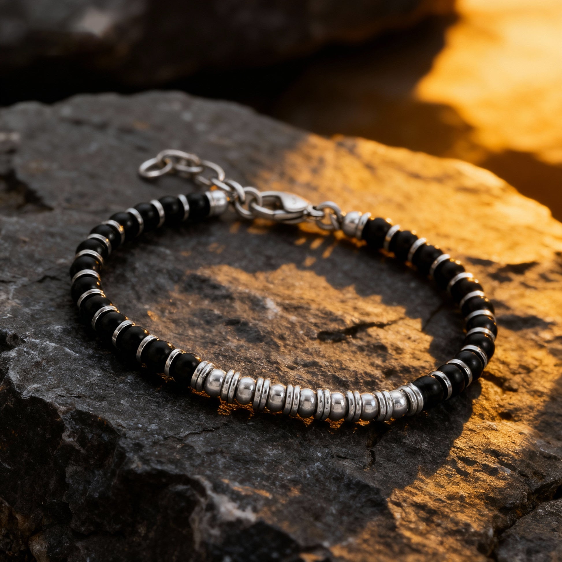 Nightfall Luxe bracelet displayed on natural rock surface, showcasing a balance of matte obsidian and lustrous steel detailing