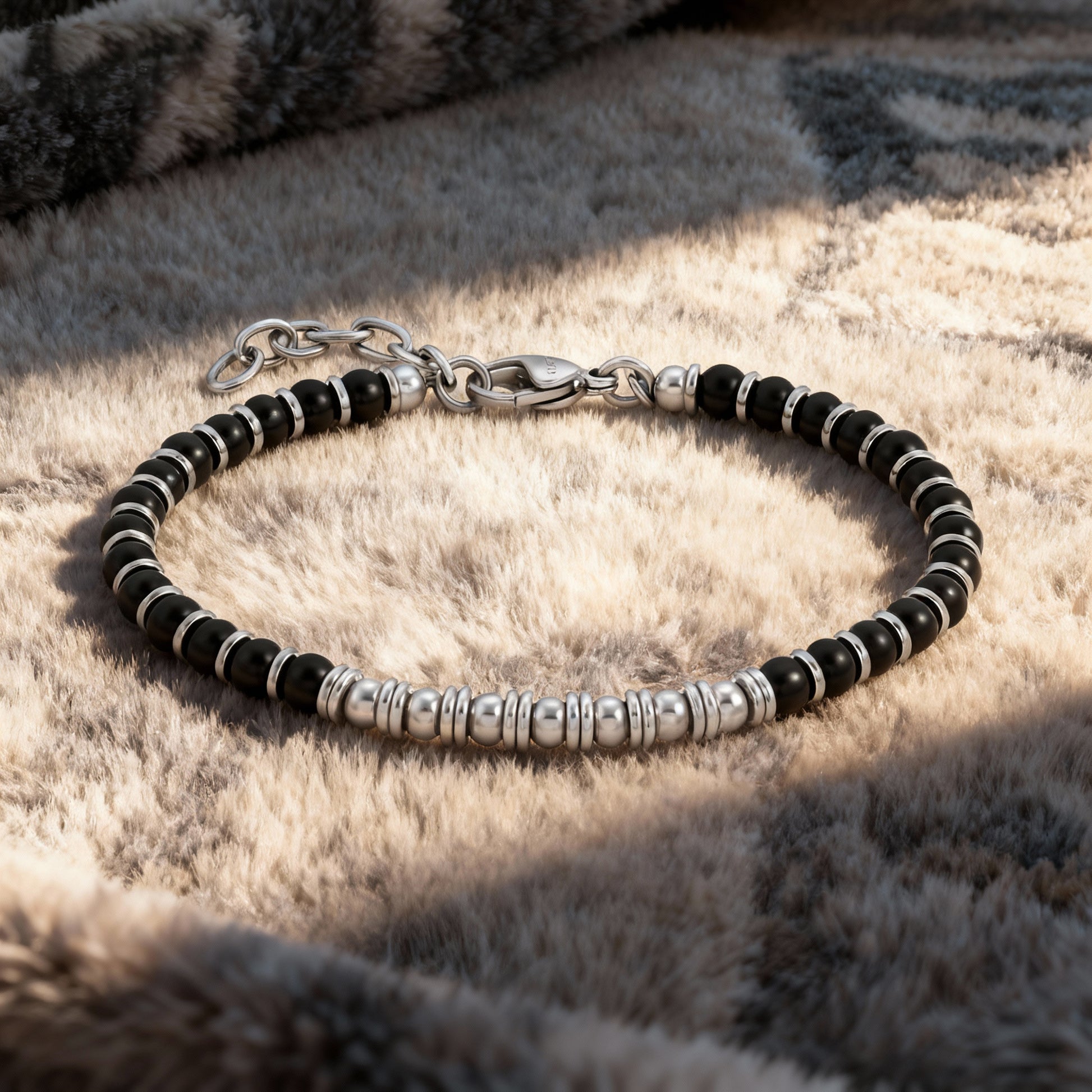 Nightfall Luxe bracelet resting on soft textured fabric, emphasizing its sophisticated mix of black obsidian stones and polished stainless-steel beads.