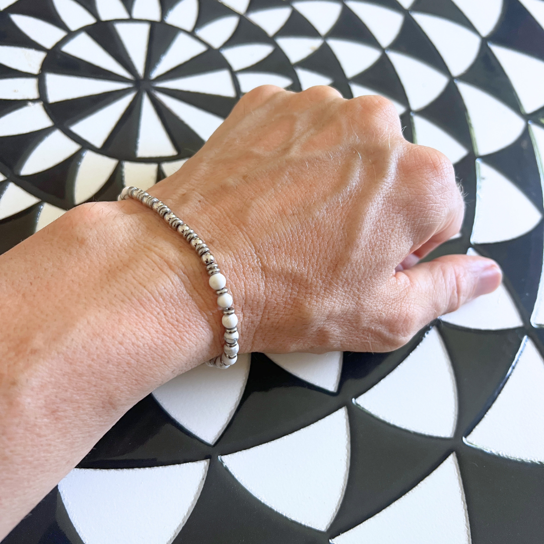 Pure Luxe white stone and stainless steel bracelet resting on a black-and-white designer mosaic table in a stylish lifestyle moment.