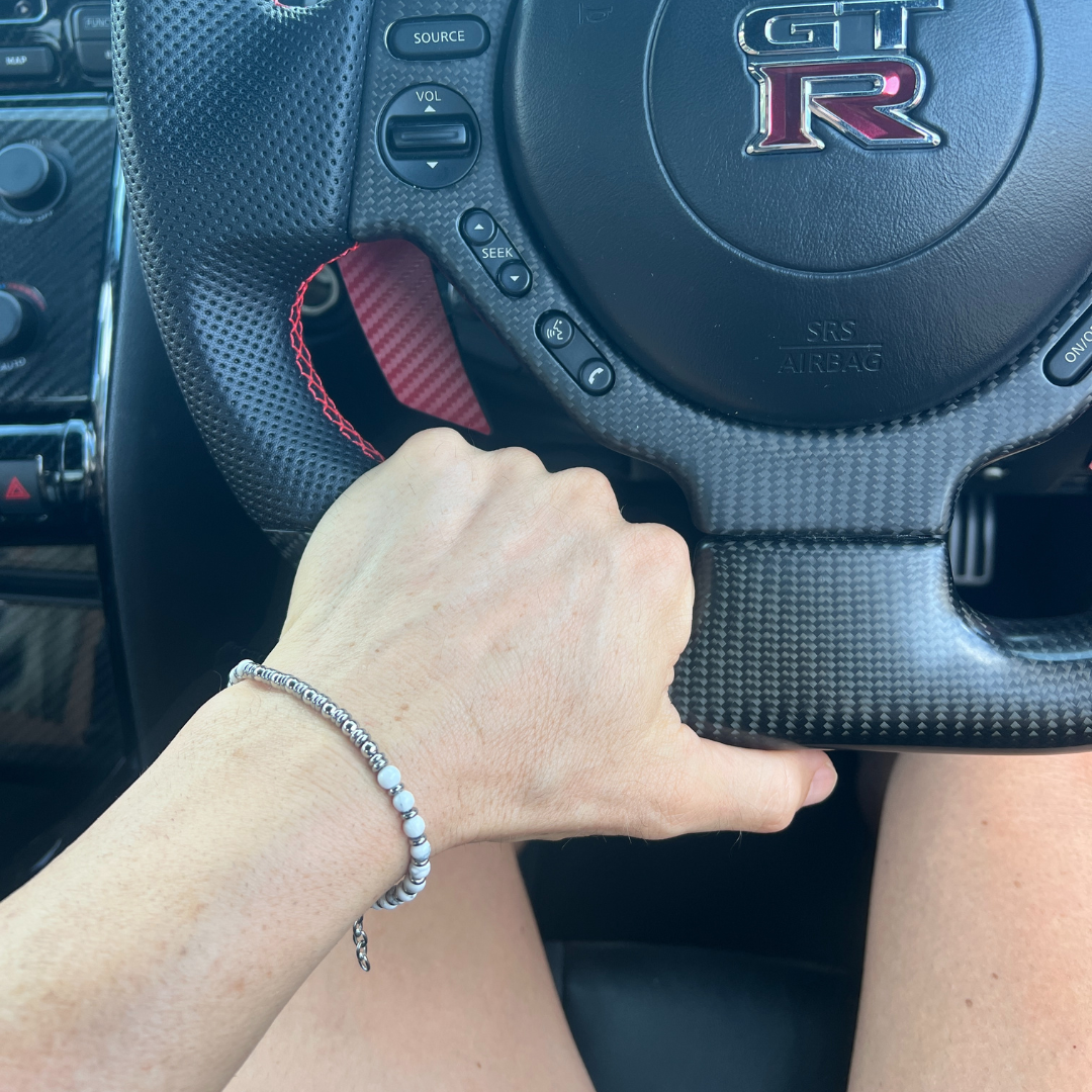 Close-up of the Pure Luxe bracelet on wrist gripping a GT-R steering wheel — blending style, performance, and refined detail.