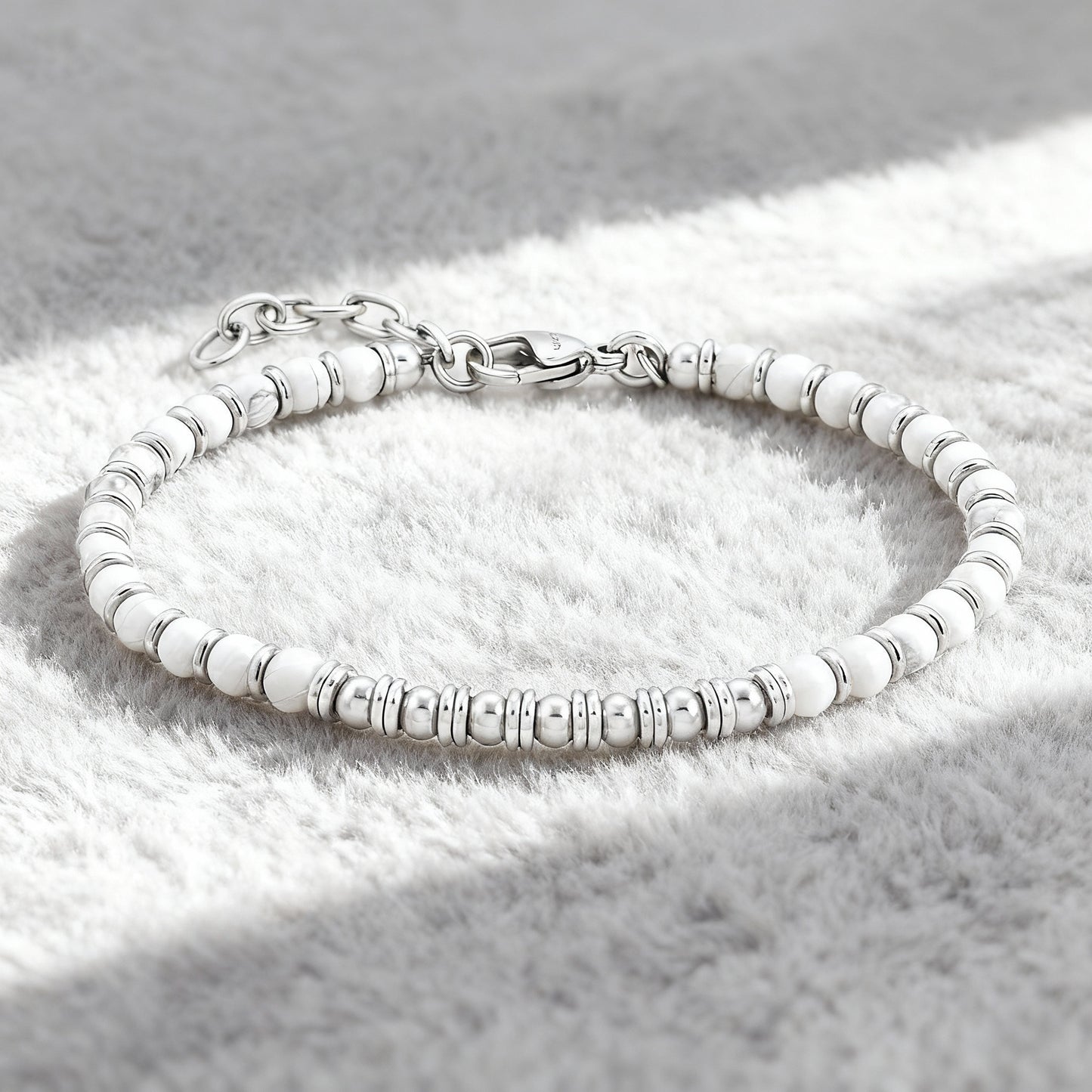 Pure Luxe bracelet featuring white howlite stones and polished stainless-steel spacers displayed on soft grey fabric background.