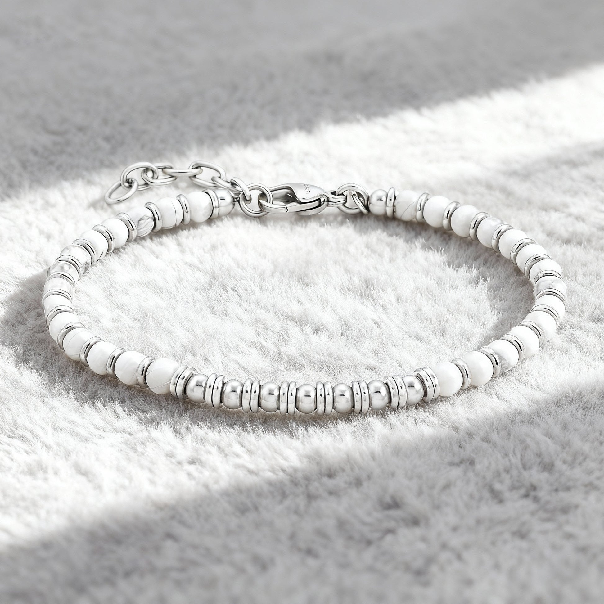 Pure Luxe bracelet featuring white howlite stones and polished stainless-steel spacers displayed on soft grey fabric background.