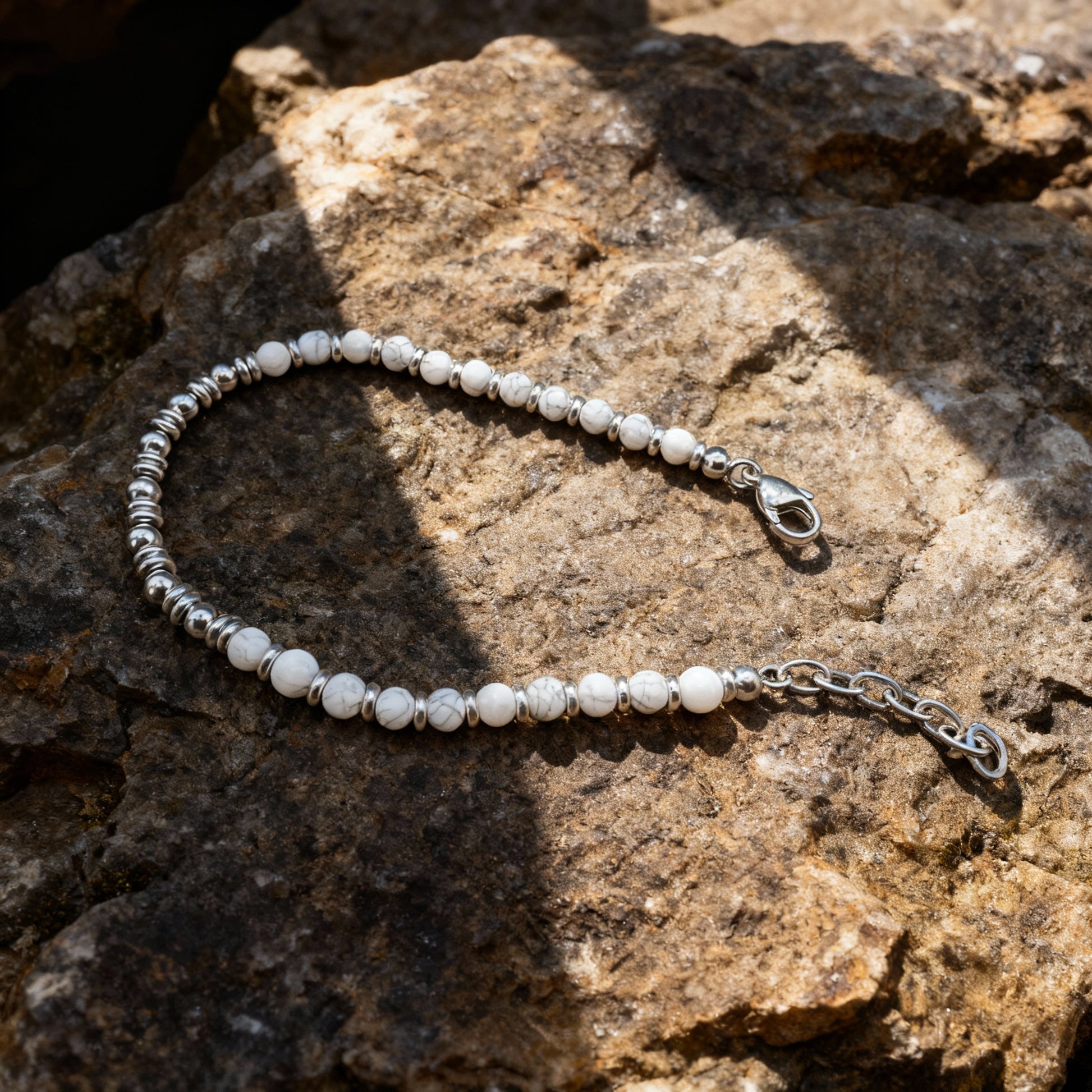 Pure Luxe bracelet laid on natural rock surface showcasing white howlite stones and silver stainless-steel spacers in sunlight.