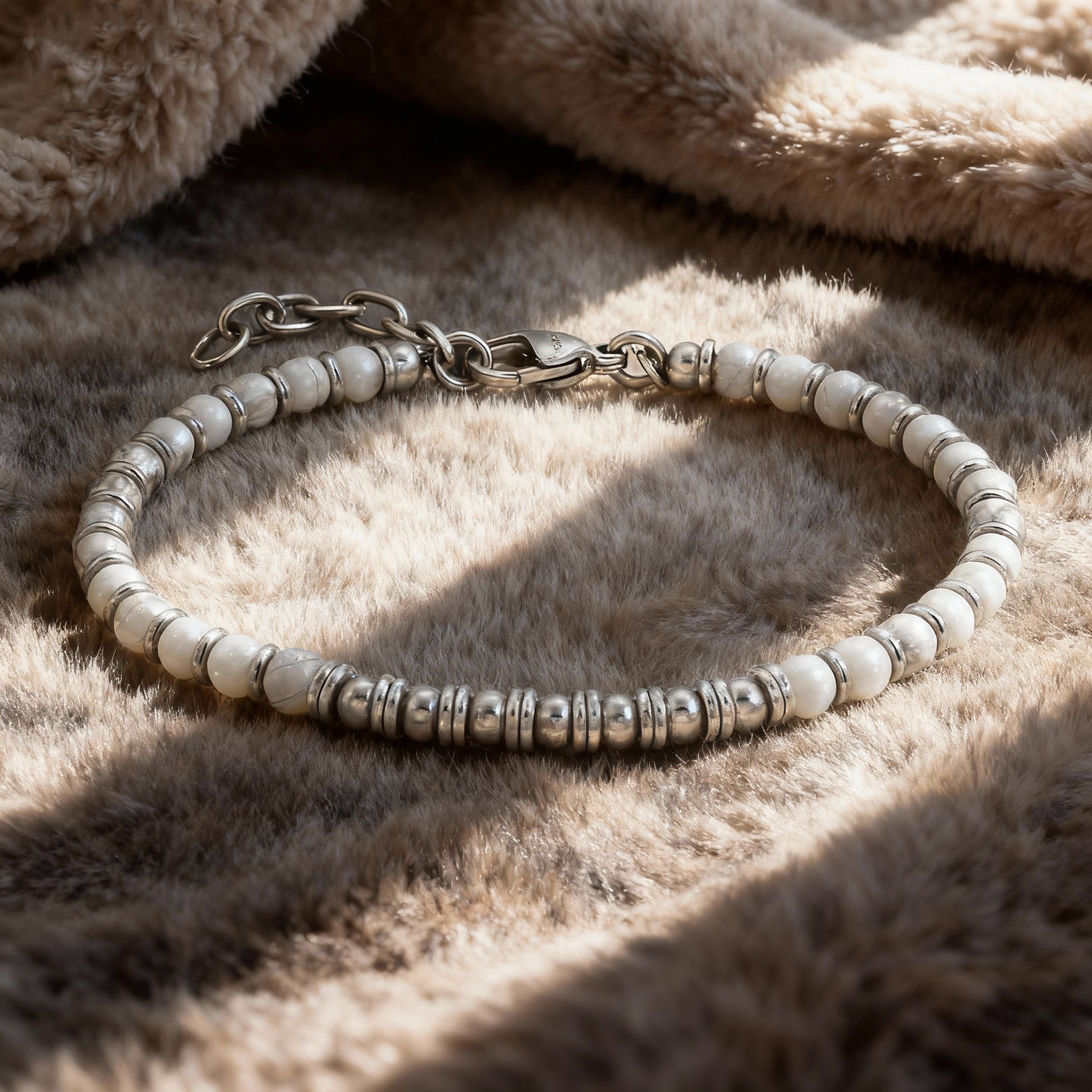 Pure Luxe bracelet with white howlite beads and stainless-steel accents displayed on soft beige fabric in warm sunlight.