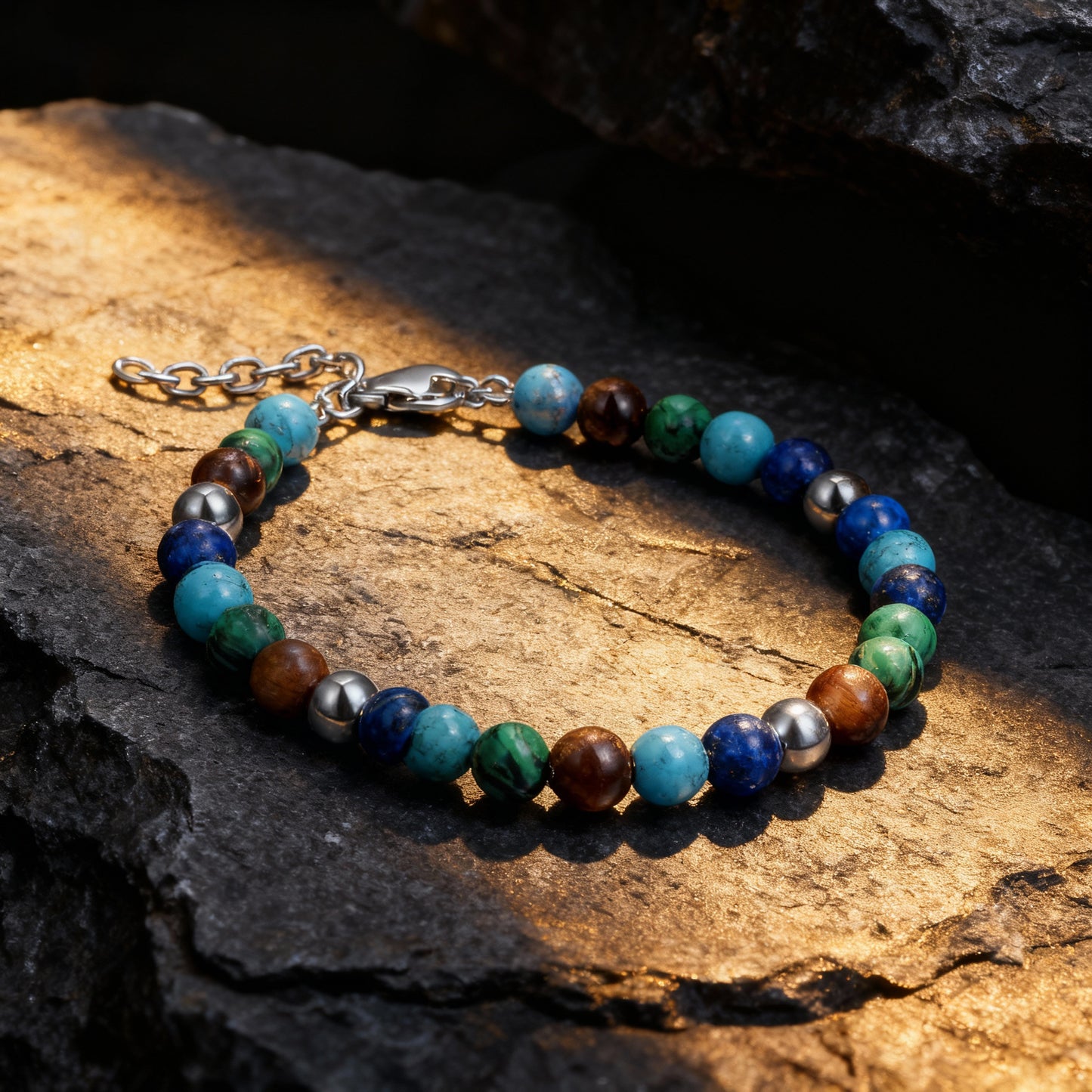 Spectrum Luxe bracelet captured under golden light on textured rock, showcasing blue, turquoise, green malachite, and tiger eye stones in a balanced design.
