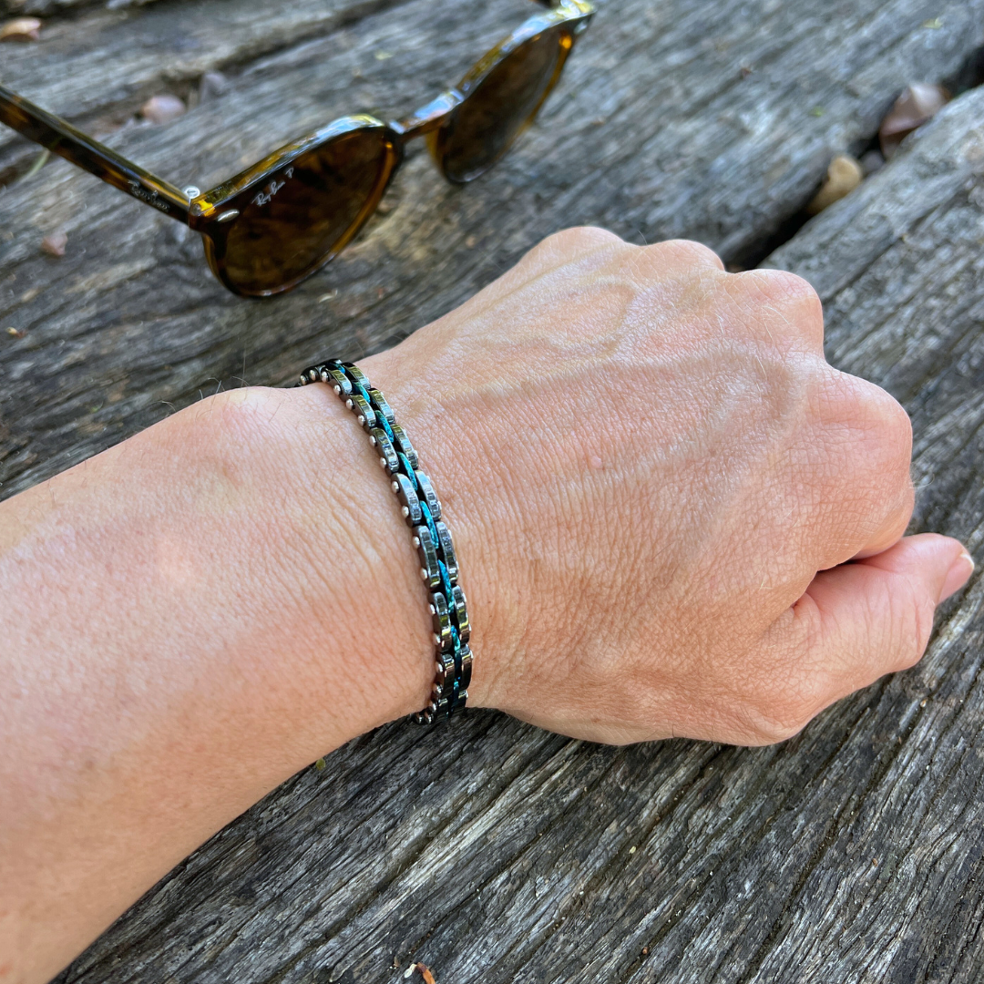 Double chain Velocity bracelet in blue and black stainless steel, styled on wrist with wood background and Ray-Ban sunglasses nearby.