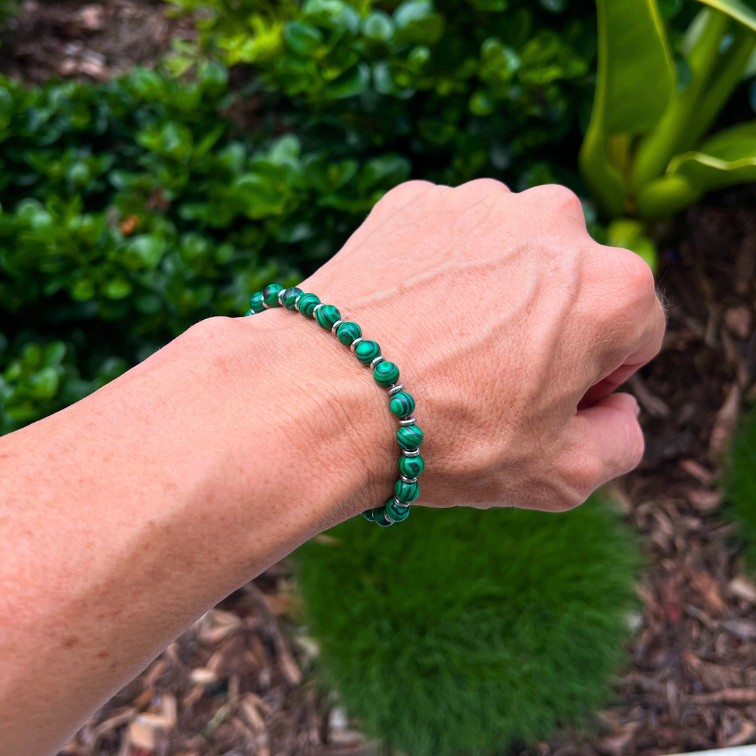 Verdure green malachite stone bracelet worn on wrist in garden setting, featuring natural patterned beads and stainless steel spacers