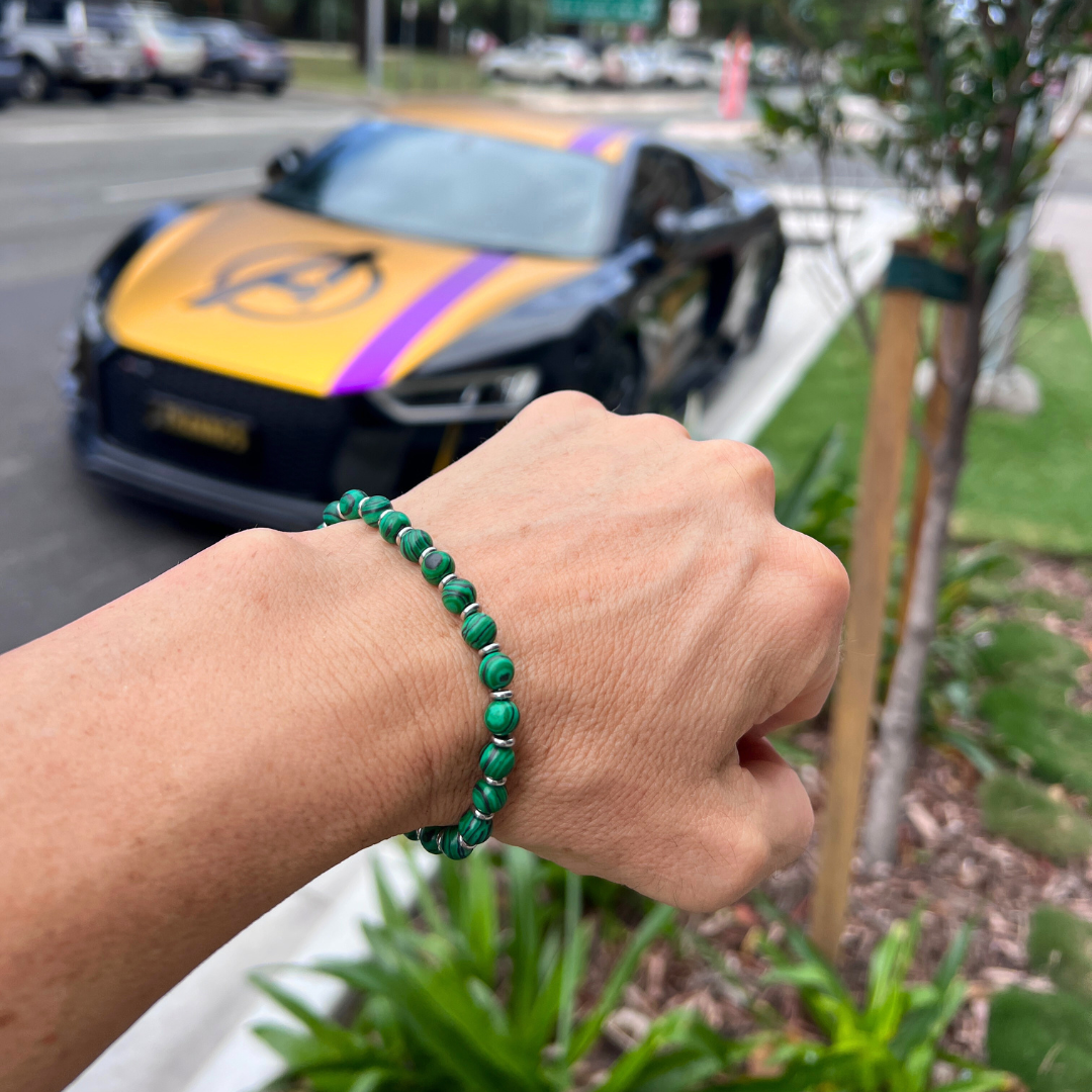 Verdure malachite bead bracelet on wrist outdoors with Audi R8 luxury car in background, green natural stone beads with stainless steel spacers.