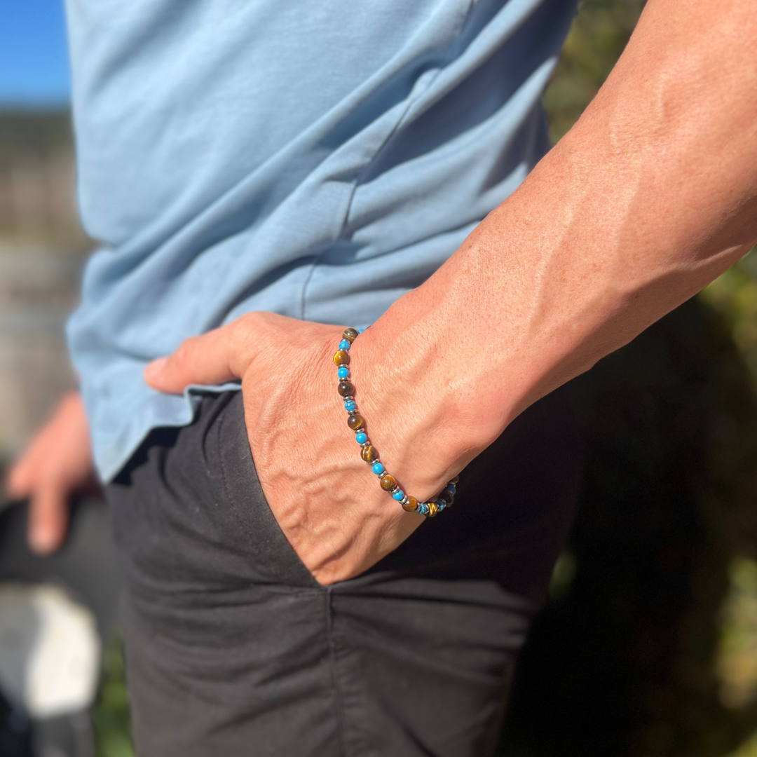 Side profile of a man wearing the Wild Oasis bracelet, featuring tiger eye and turquoise beads, with his hand in his pocket under bright outdoor sunlight.